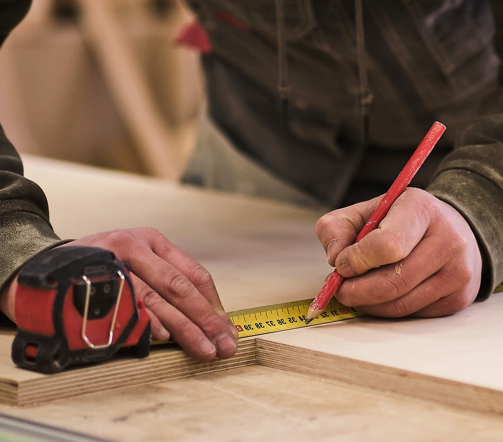 Treated Lumber Products | Man measuring piece of wood with pencil and tape measure | BB&S Lumber